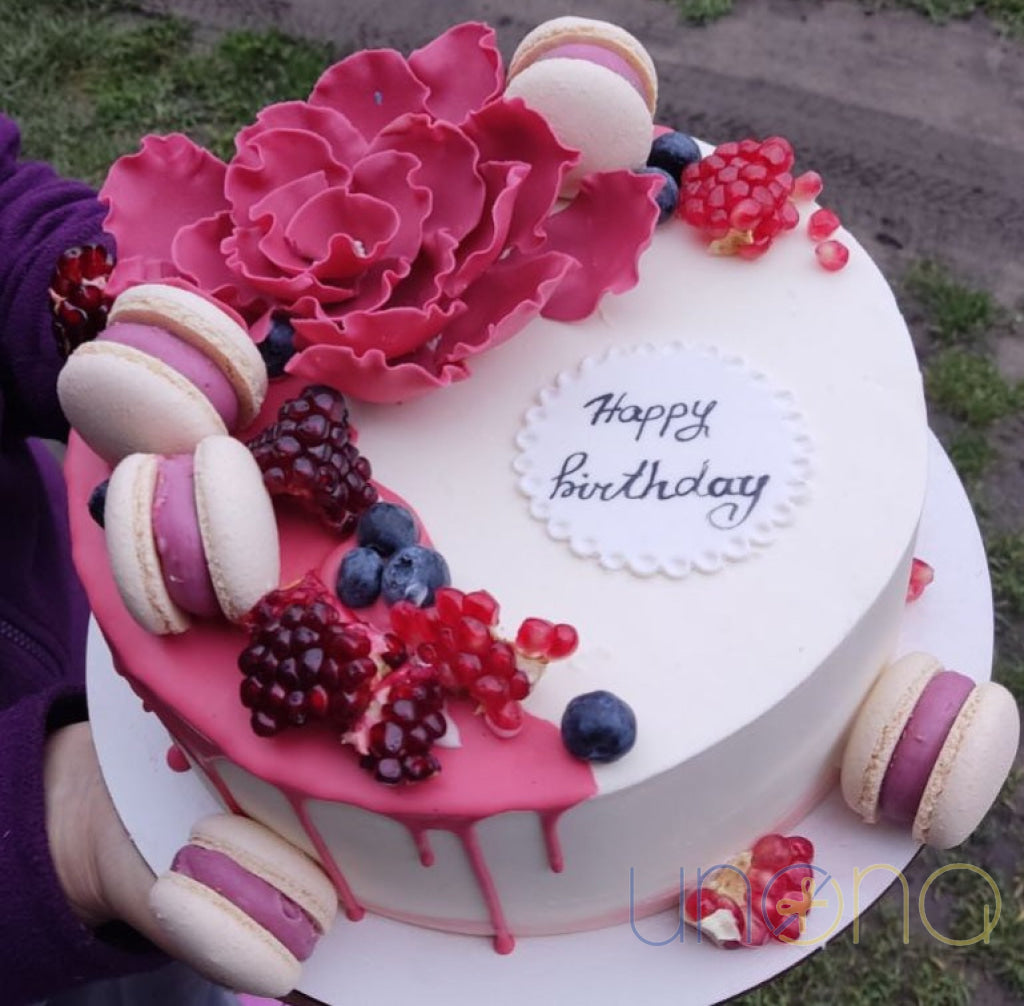 Birthday cake topped with fresh strawberries, raspberries and blueberries and macarons