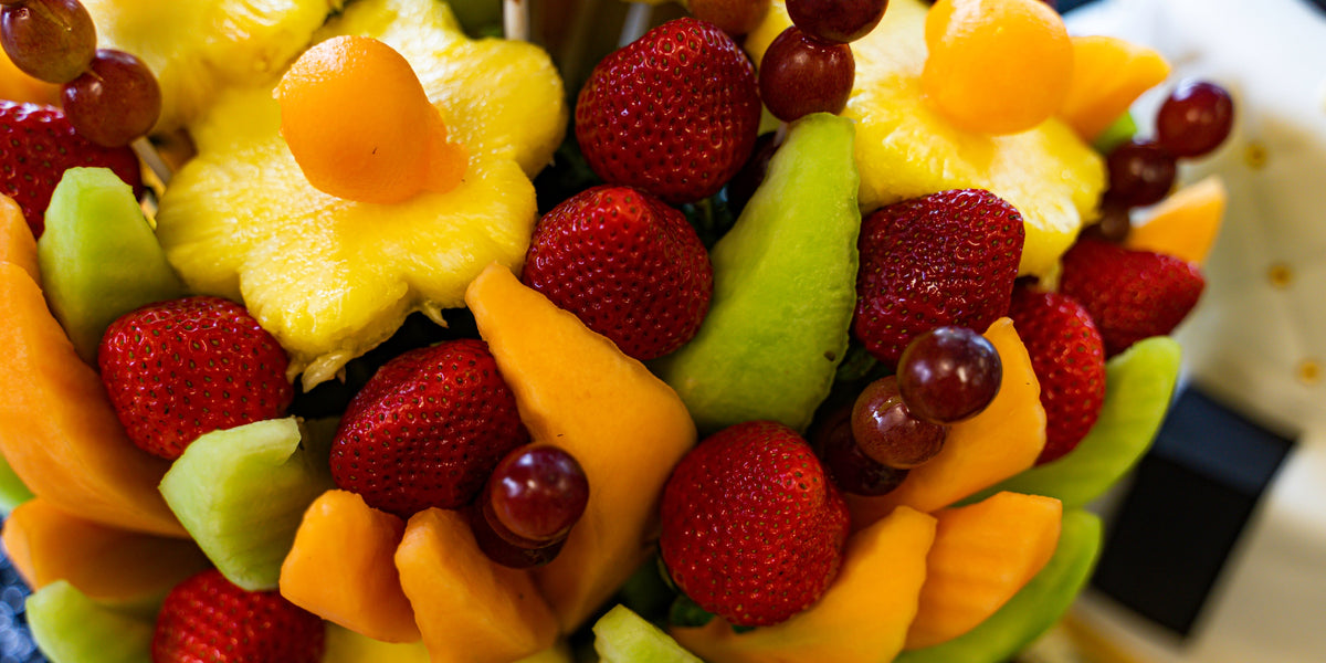 Fruit arrangement with pineapple flowers, strawberries, red grapes, and orange and green melon slices